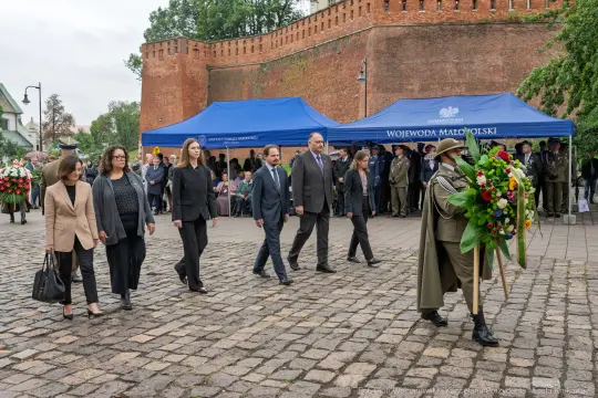Uroczystość złożenia kwiatów przy pomniku, uczestnicy w formalnych strojach.