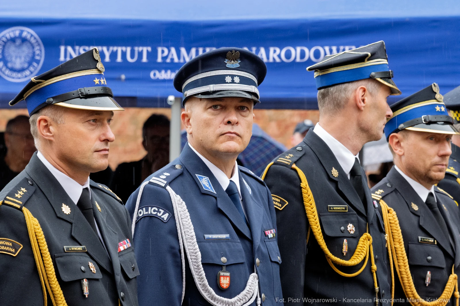 Czterech mężczyzn w mundurach policyjnych podczas ceremonii, z tłem namiotu instytucji.  Autor: Piotr Wojnarowski