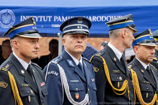 Czterech mężczyzn w mundurach policyjnych podczas ceremonii, z tłem namiotu instytucji.