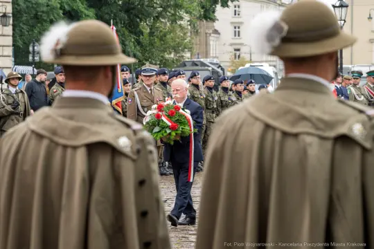 Mężczyzna składa wieniec w towarzystwie żołnierzy i innych uczestników uroczystości.