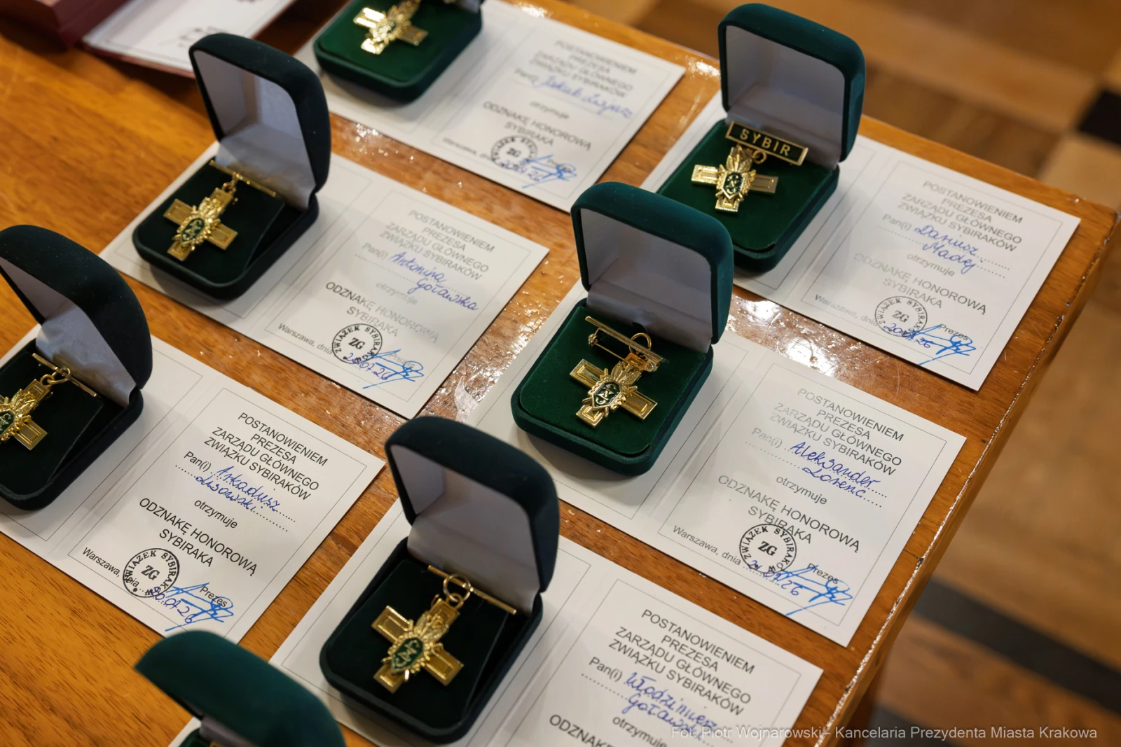 Złote krzyże honorowe w otwartych pudełkach na tle dyplomów.  Autor: Piotr Wojnarowski