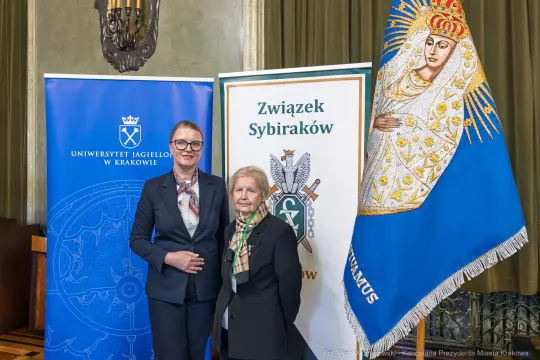 Dwie kobiety stoją obok siebie, w tle flagi Uniwersytetu Jagiellońskiego i Związku Sybiraków.