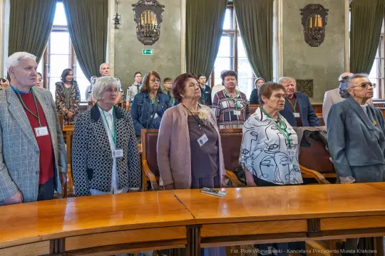 Grupa osób stojących w sali, uczestniczących w wydarzeniu.