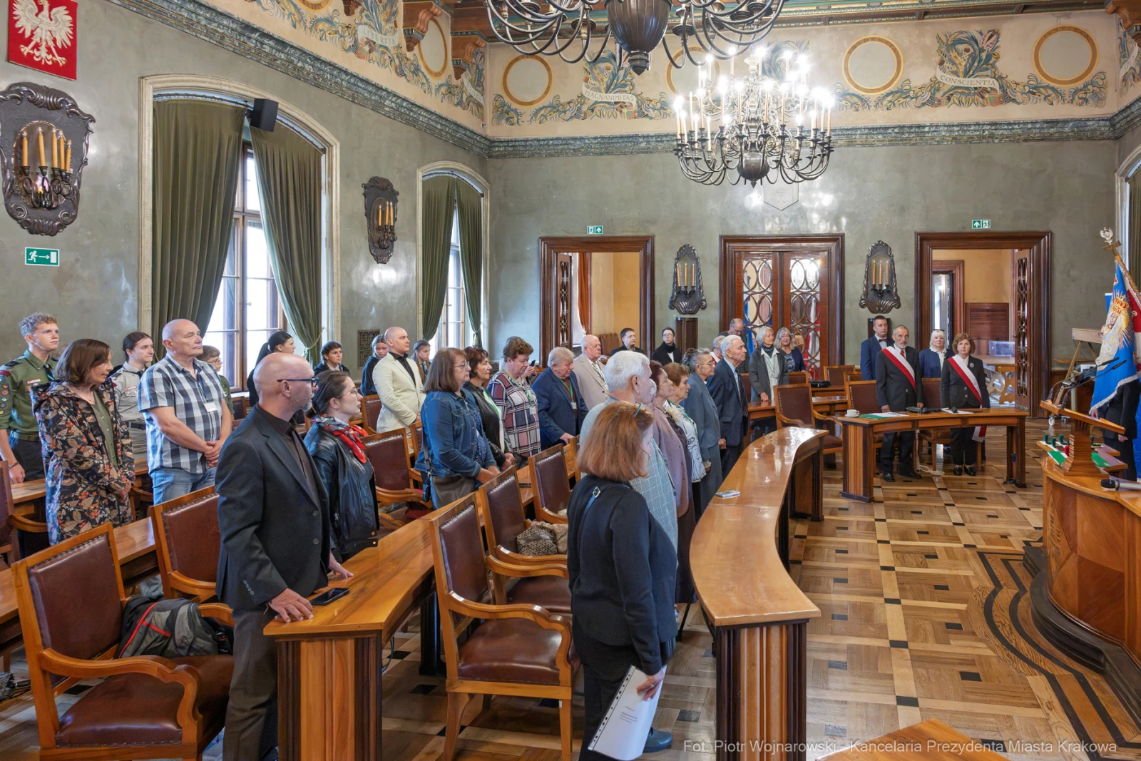 Uczestnicy ceremonii stoją w sali obrad, w tle flagi i herb miasta.  Autor: Piotr Wojnarowski