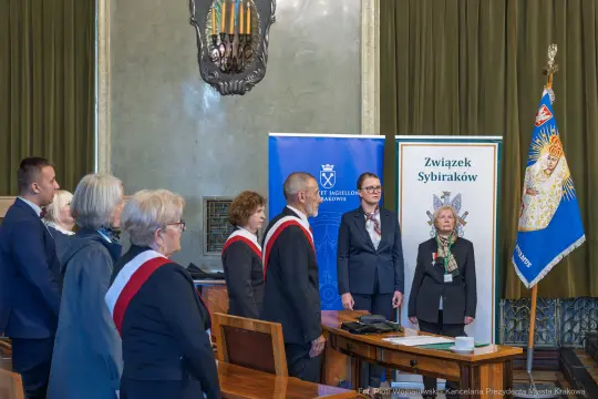 Ceremonia wręczenia odznaczeń członkom Związku Sybiraków w sali z flagami i emblematami.