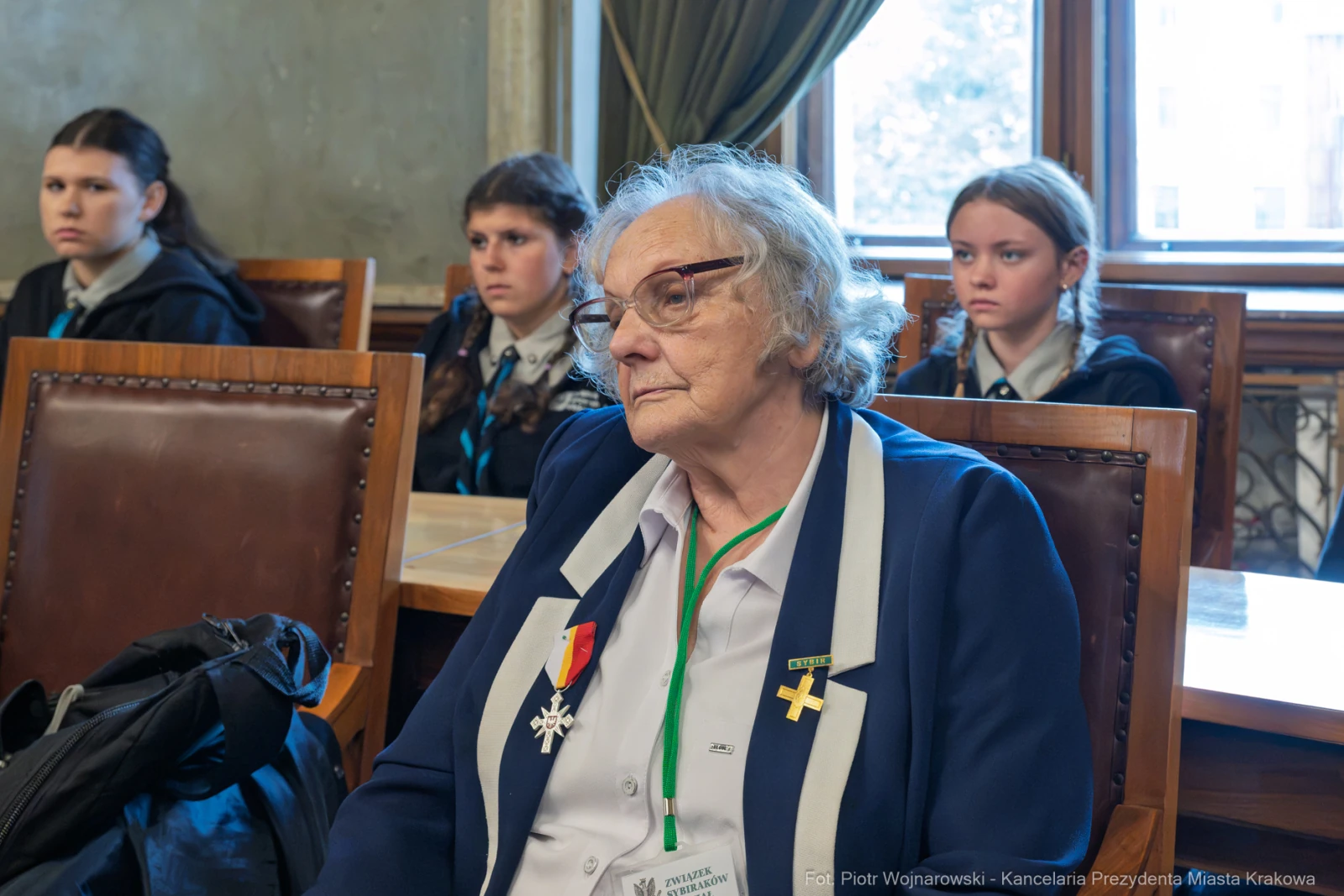 Starsza kobieta w garniturze z odznaczeniem, siedzi w sali obrad, w tle młodzież.  Autor: Piotr Wojnarowski
