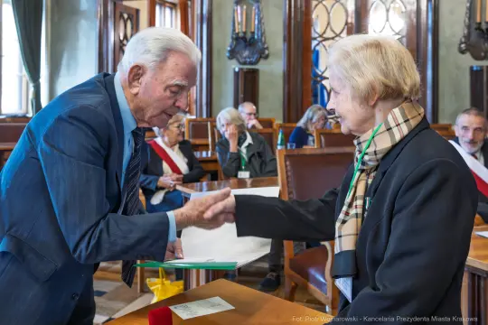 Uroczystość wręczenia odznaczeń w sali obrad z uczestnikami w tle.