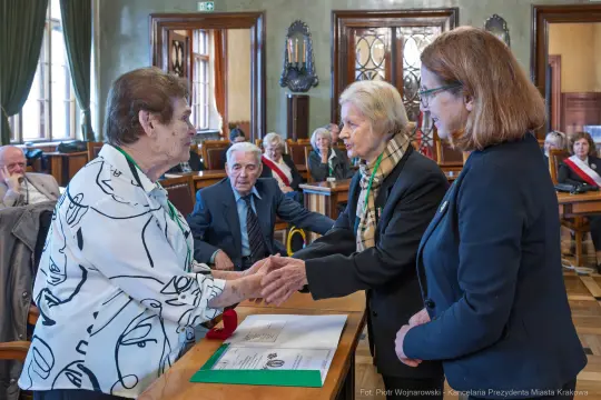 Wręczenie odznaczeń w sali obrad, uczestnicy w formalnych strojach.