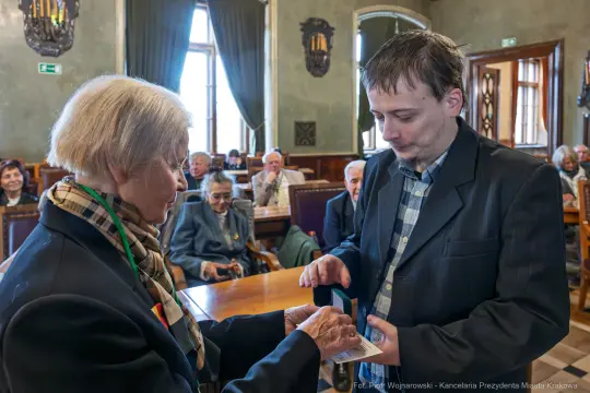 Wręczenie odznaczenia przez kobietę mężczyźnie w sali z publicznością.