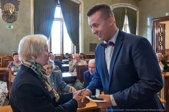 Uroczystość wręczenia odznaczeń w sali obrad z uśmiechniętymi uczestnikami.