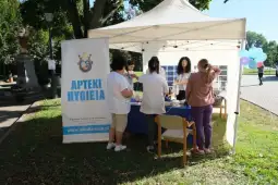 Stoisko apteki z pracownikami, którzy obsługują klientów w parku. Balony w tle.