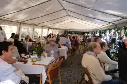 Spotkanie seniorów w namiocie, przy stołach z jedzeniem i napojami.