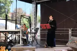 Kobieta w eleganckiej sukni recytuje tekst na scenie, obok mężczyzna przy keyboardzie.