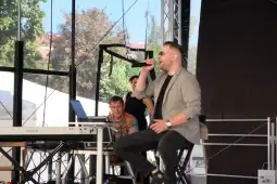 Mężczyzna śpiewający na scenie, obok muzycy przy instrumentach.