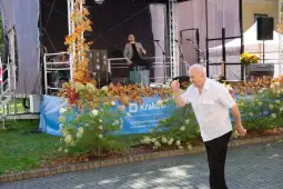 Mężczyzna tańczący przed sceną z muzykami w tle, otoczony kolorowymi liśćmi.