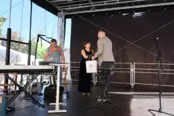 Wręczenie nagrody na scenie, uczestnicy w eleganckich strojach.