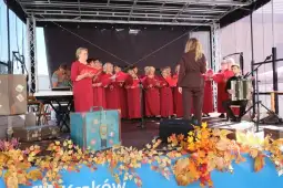 Chór w czerwonych strojach występuje na scenie, akompaniament na akordeonie.