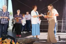 Grupa osób na scenie podczas wydarzenia, jedna z nich wręcza nagrodę.