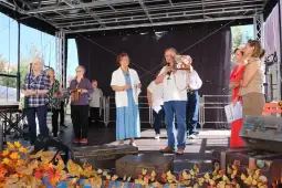 Grupa osób na scenie podczas wydarzenia, jedna osoba trzyma domowy przedmiot.