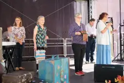 Cztery osoby na scenie, jedna z mikrofonem, pozostałe z przedmiotami w rękach.