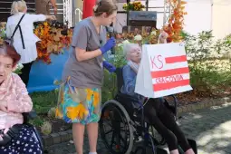 Kobieta na wózku inwalidzkim trzyma plakat z napisem KS Cracovia, obok stoi opiekunka.