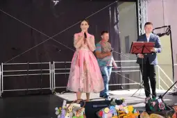 Kobieta w różowej sukience śpiewa na scenie, obok mężczyźni z instrumentami.