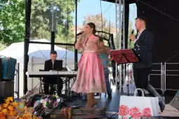 Występ artystów na scenie, kobieta w różowej sukience śpiewa, mężczyzna towarzyszy jej przy mikrofonie.