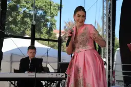 Kobieta w różowej sukni śpiewa na scenie, obok niej muzyk gra na fortepianie.