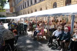 Grupa osób starszych siedzących pod namiotem, uczestniczących w wydarzeniu na świeżym powietrzu.