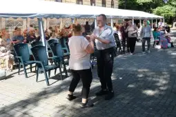 Para tańczy na świeżym powietrzu, w tle siedzi grupa ludzi.