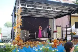 Występ artystyczny na scenie z kwiatami w tle.