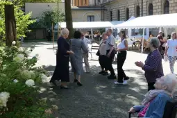 Grupa osób tańczących i bawiących się w ogrodzie, w tle stoiska z jedzeniem.