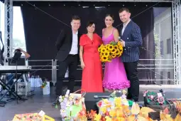 Cztery osoby na scenie, jedna z bukietem słoneczników, w tle dekoracje i instrumenty muzyczne.