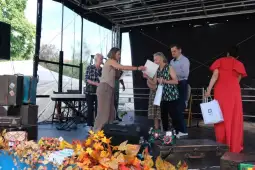 Wręczenie nagród na scenie podczas wydarzenia, z uczestnikami i dekoracjami w tle.