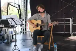 Młody muzyk grający na gitarze akustycznej podczas występu na scenie.