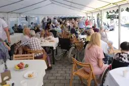 Spotkanie seniorów w plenerze, stoły z jedzeniem, wiele osób w różnych aktywnościach.