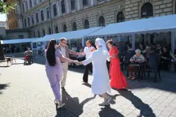 Grupa osób tańczących na zewnątrz, w tle widoczni obserwatorzy.