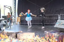 Dzieci tańczą na scenie, jedno z nich trzyma koszyk, drugie w eleganckim stroju.