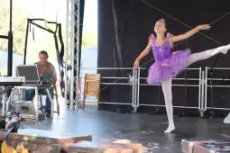 Baletnica w fioletowej sukience tańczy na scenie, obok siedzi muzyk przy keyboardzie.