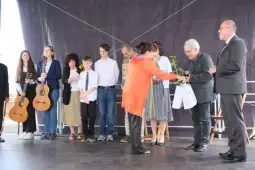 Uroczystość wręczenia nagród, uczestnicy z instrumentami i kwiatami na scenie.