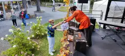 Mężczyzna w kolorowej koszuli odbiera nagrodę od kobiety na scenie podczas wydarzenia plenerowego.