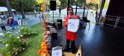 Kobieta w czerwonej sukience trzyma torby na tle sceny i publiczności.