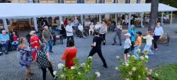 Grupa osób tańczących na świeżym powietrzu, w tle widoczna restauracja i zieleń.