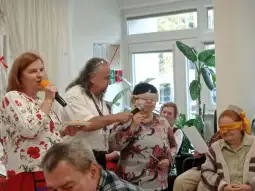 Osoby w sali bawią się w grze z zasłoniętymi oczami, jedna z nich trzyma mikrofon.