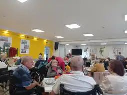 Spotkanie osób starszych w świetlicy, przy stole z napojami i przekąskami.