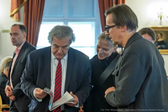 Grupa ludzi w formalnym otoczeniu, przeglądających dokumenty i rozmawiających.