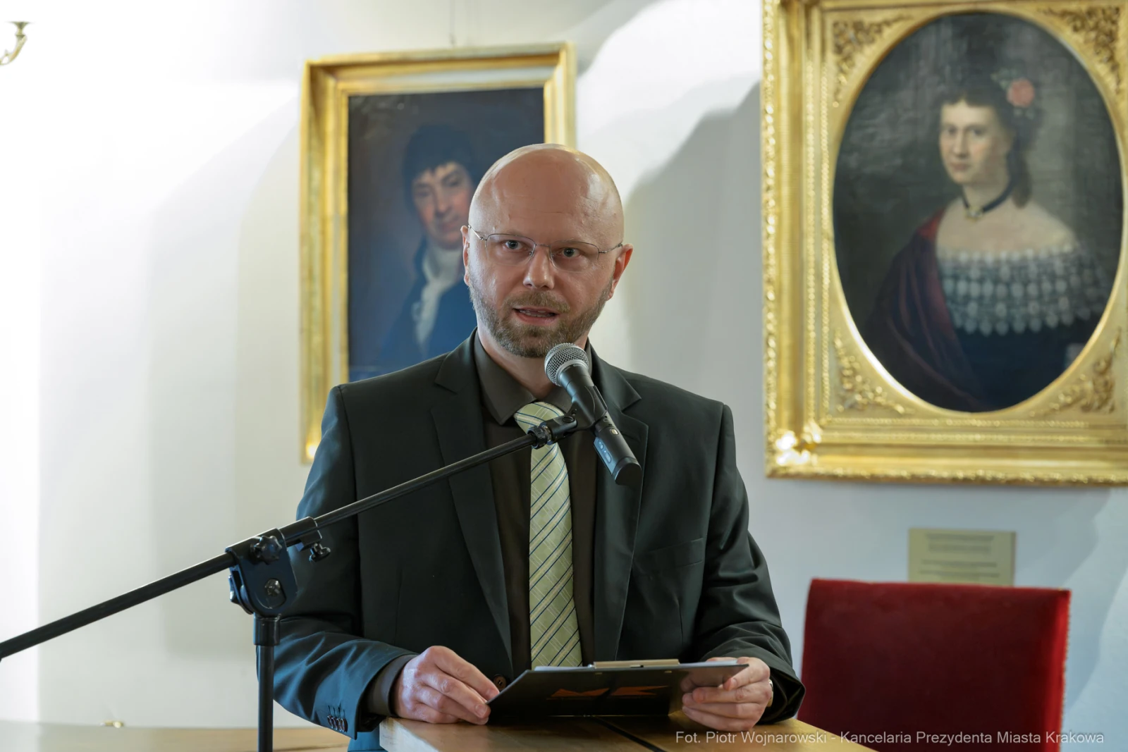 Mężczyzna przemawia przy mikrofonie w sali z obrazami w tle.  Autor: Piotr Wojnarowski