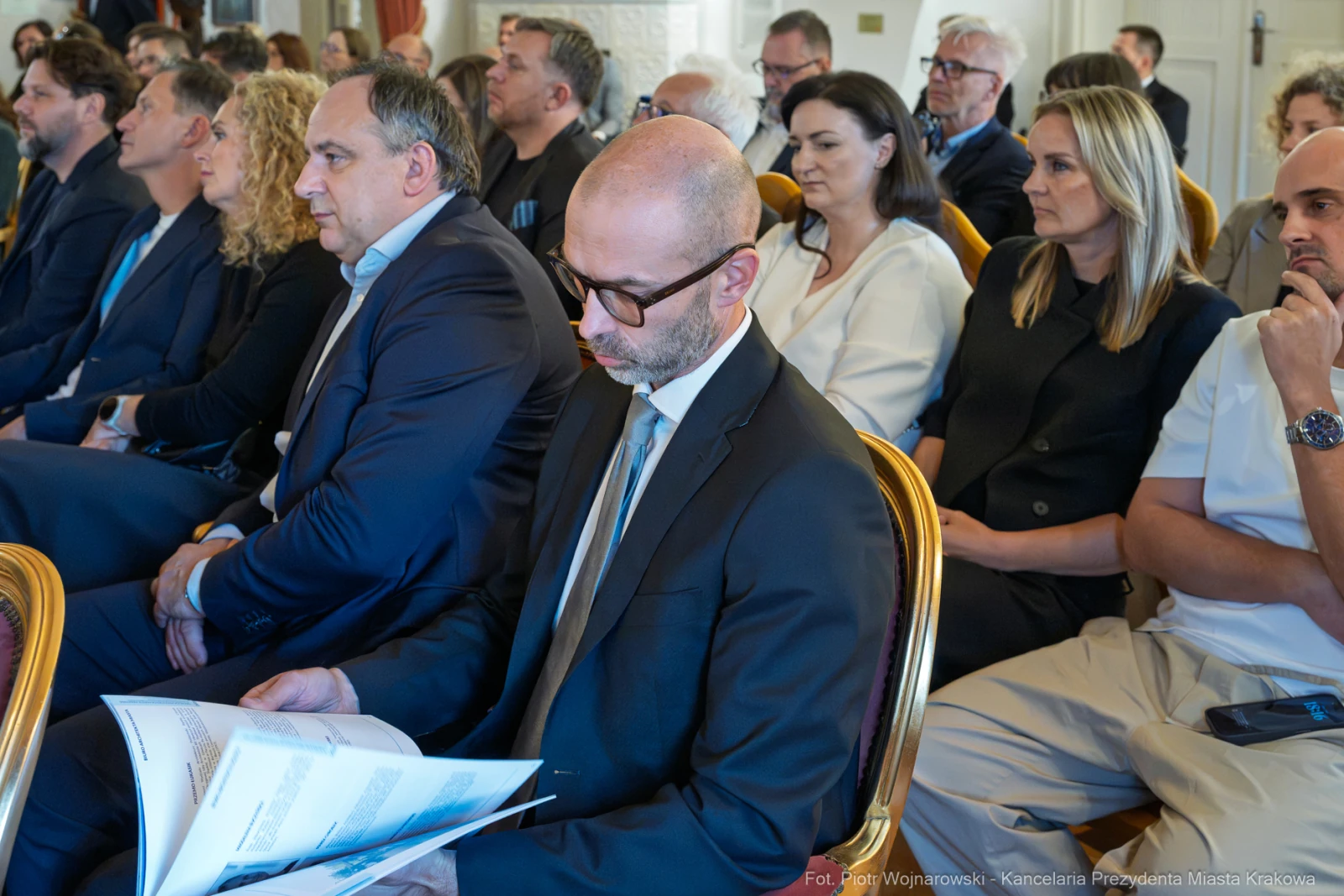 Grupa ludzi siedzących na sali, niektórzy trzymają dokumenty.  Autor: Piotr Wojnarowski