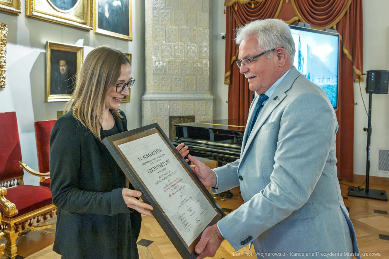 Wręczenie nagrody osobie z dyplomem w eleganckim wnętrzu.  Autor: Piotr Wojnarowski