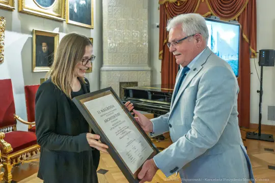 Wręczenie nagrody osobie z dyplomem w eleganckim wnętrzu.